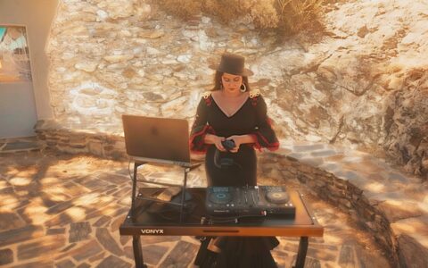 Dj flamenca en tenue noire et rouge qui mixe dans un paysage méditerranéen en extérieur.